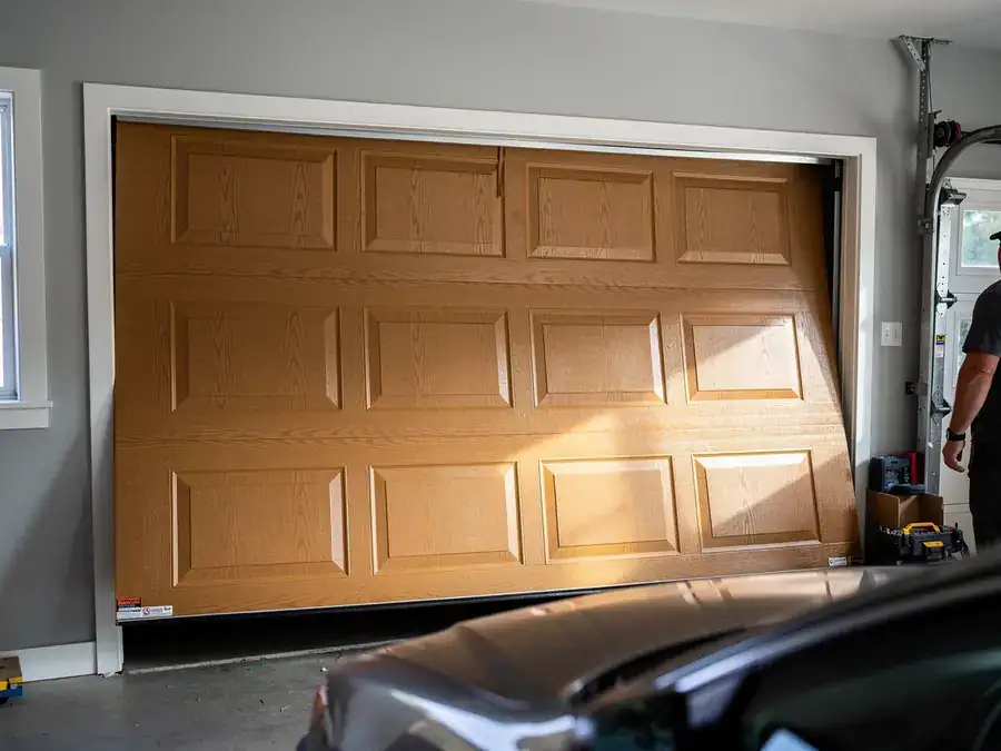 A brown garage door is crooked in its frame, with a technician standing nearby.